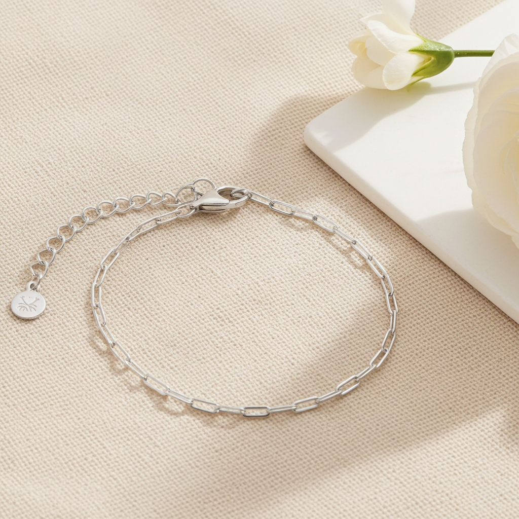 Silver paperclip bracelet on a beige surface with a white flower in the background